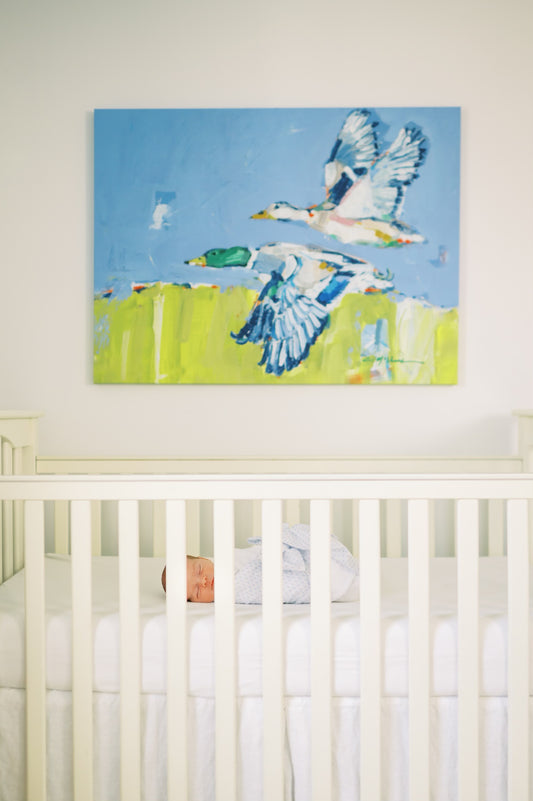 Duck canvas print featuring original artwork by Chelsea McShane displayed in a blue and white nursery above a crib with a newborn baby inside.