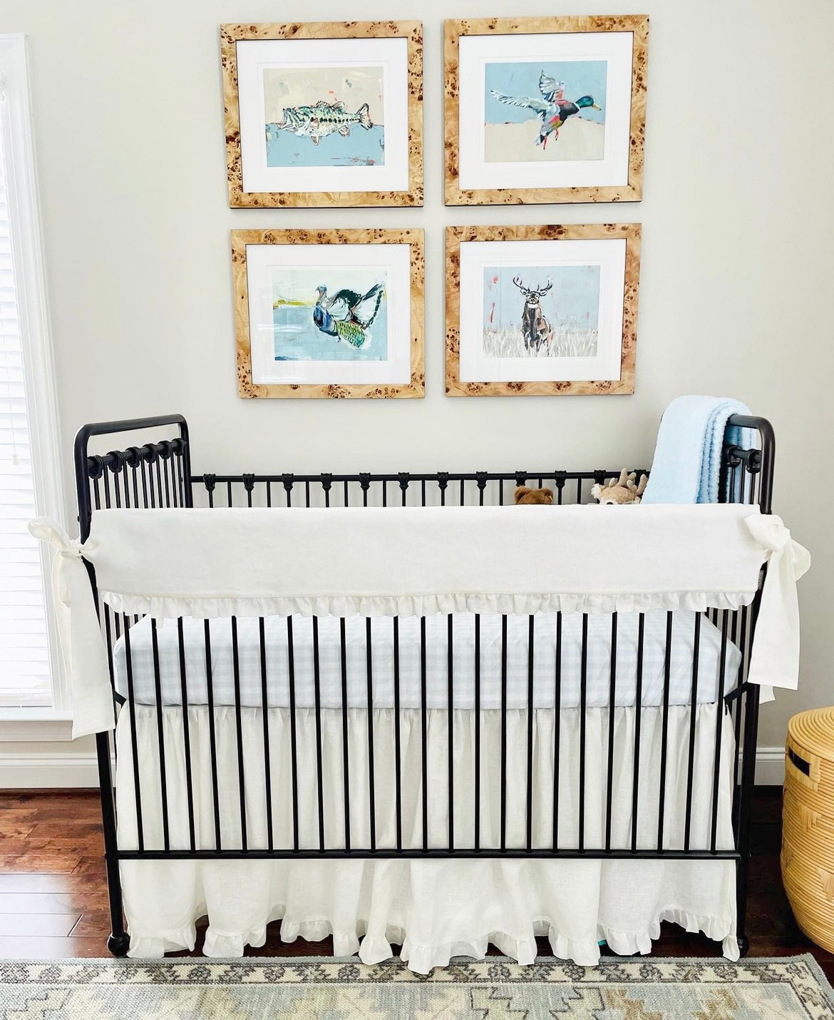 A duck, fish, turkey, and deer painting that is framed and featured in a nursery above a crib.